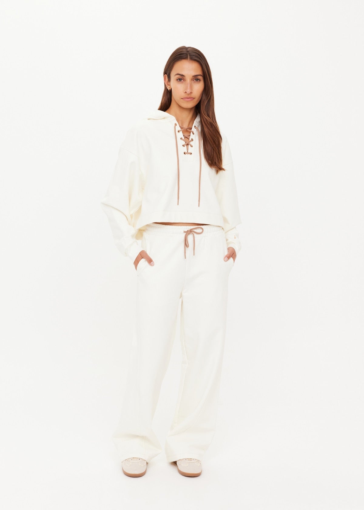 Woman wearing a cream hoodie with hands in pockets, showcasing a relaxed fit and soft material.