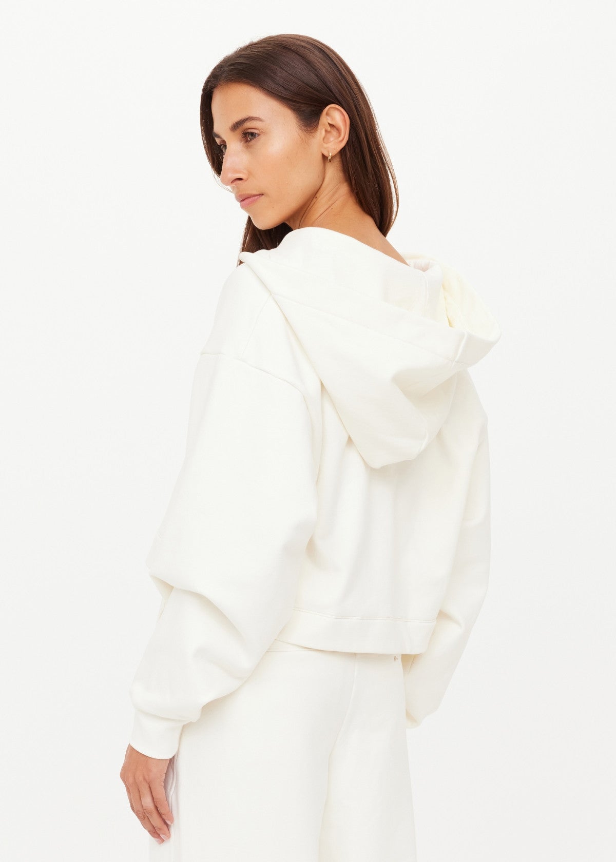 Woman wears a cream hoodie, cotton material, shown in profile with head turned, against a plain white background.