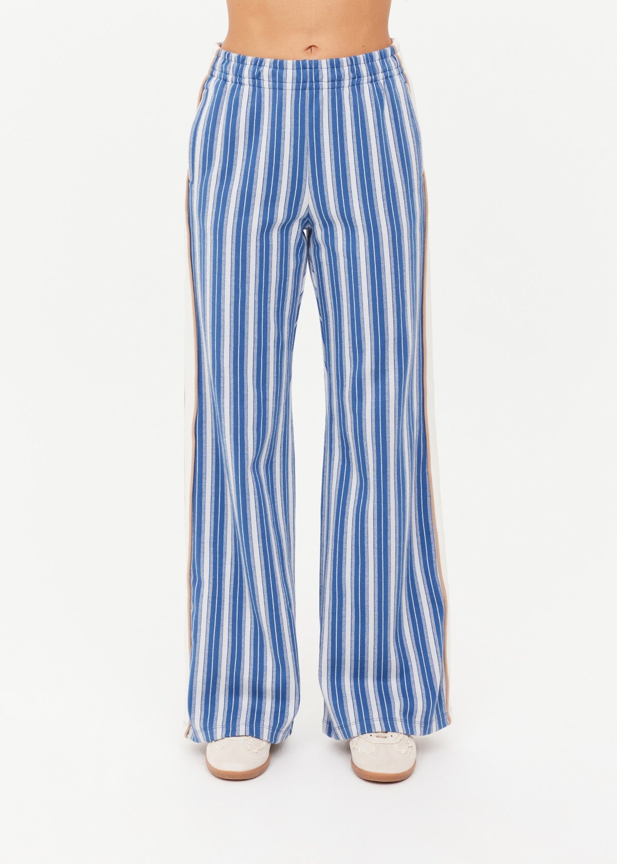 Woman wearing denim wide-leg pants with side stripes and white sneakers, shown from the front.