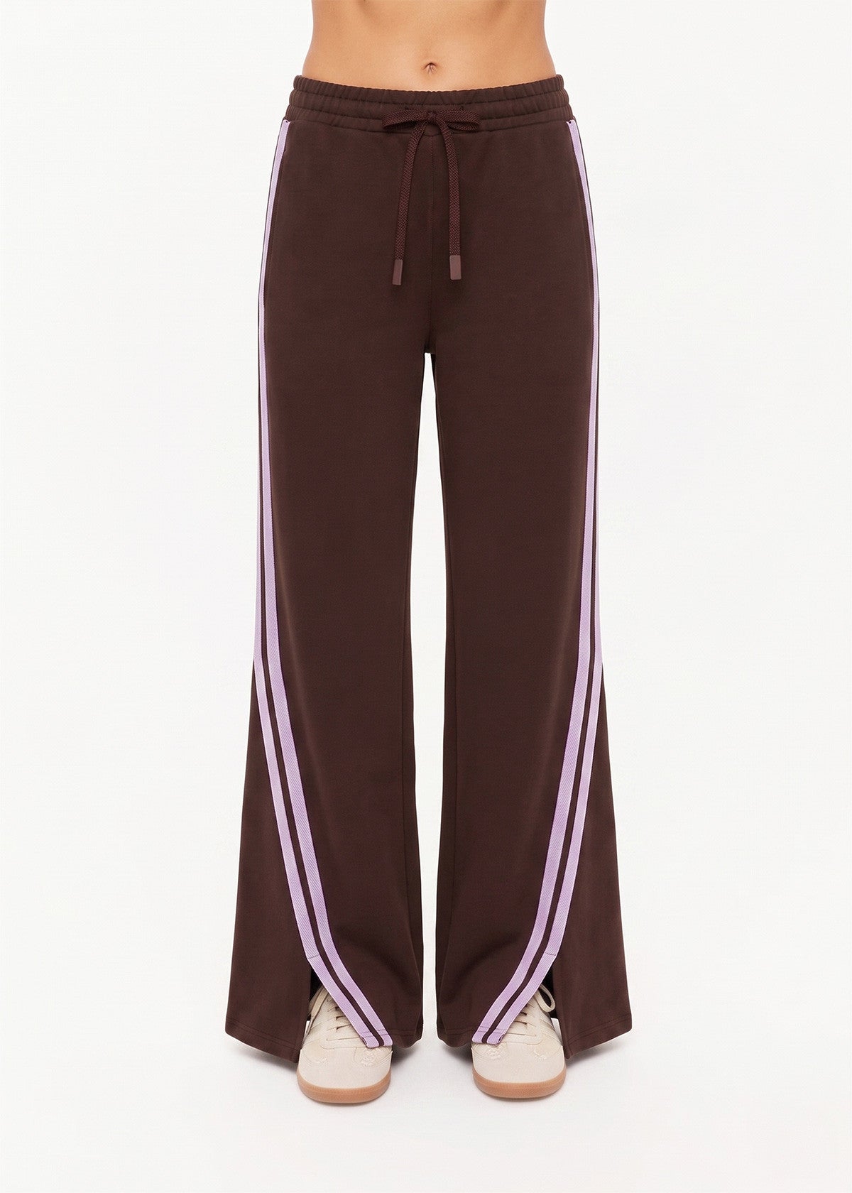 High-waisted cocoa pants with lilac mesh panels, purple stripes, drawstring waist; paired with beige sneakers.