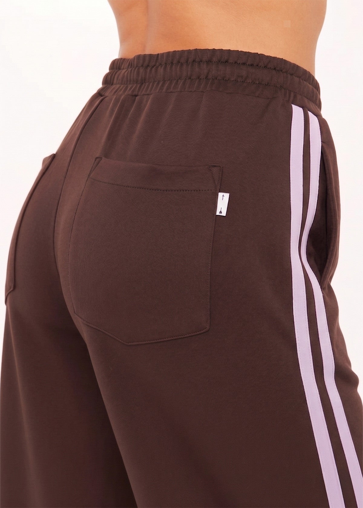 High-waisted cocoa track pants with white side stripes, visible waistband, and back pocket. Suitable for casual wear.