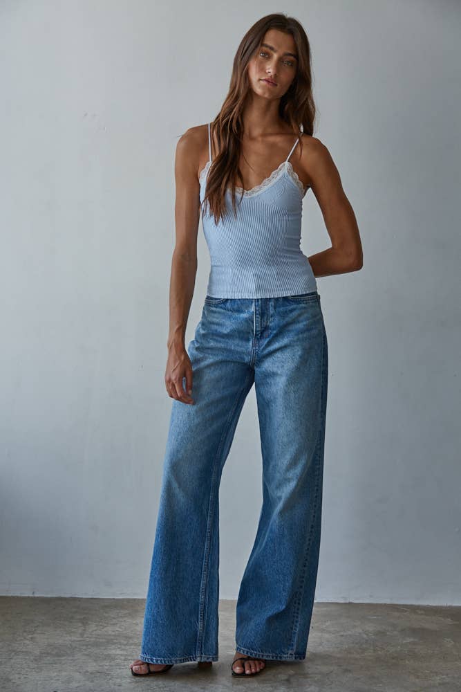 Woman wears a pale blue knit top and wide-leg denim jeans, standing against a simple light backdrop.