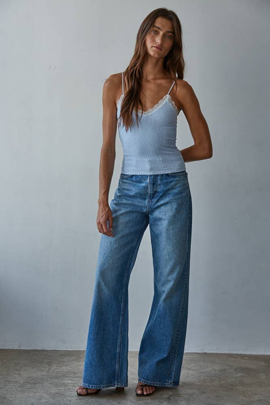 Woman wears a pale blue knit top and wide-leg denim jeans, standing against a simple light backdrop.