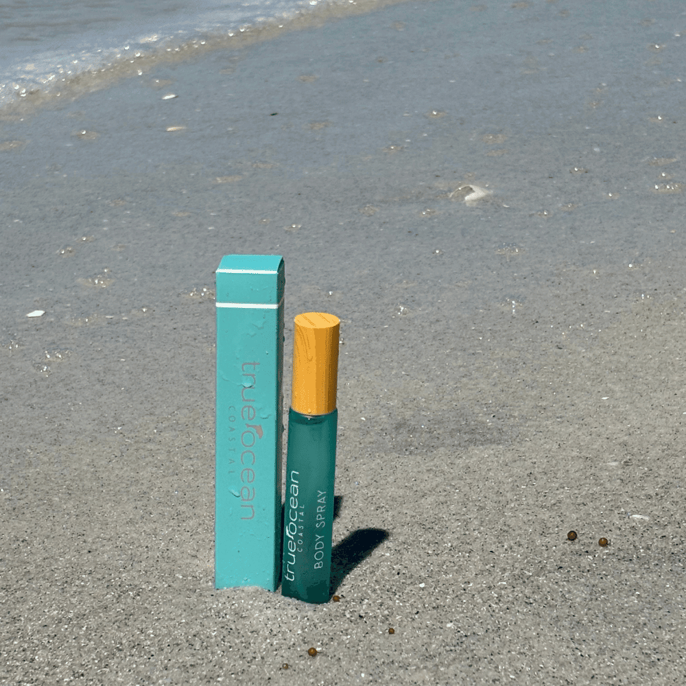 Blue Ocean body spray bottle stands upright on sandy beach, plastic packaging designed for outdoor fragrance use.