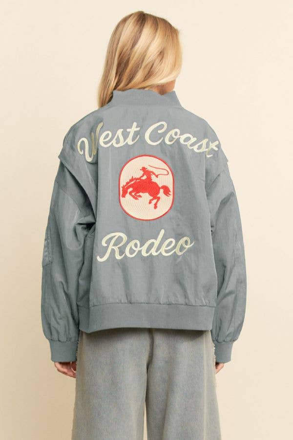 Blonde woman in a black embroidered bomber jacket with red rodeo graphic on the back, suitable for casual wear.
