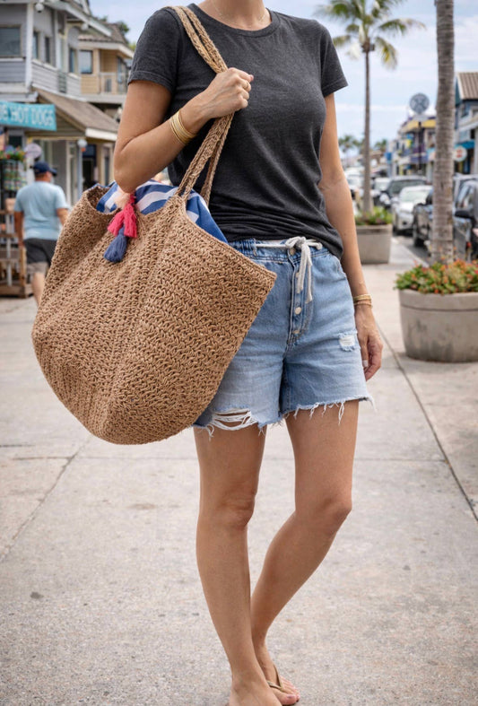 Woman in black tee and denim shorts carries a large neutral canvas tote bag suitable for everyday use on a sunny street.