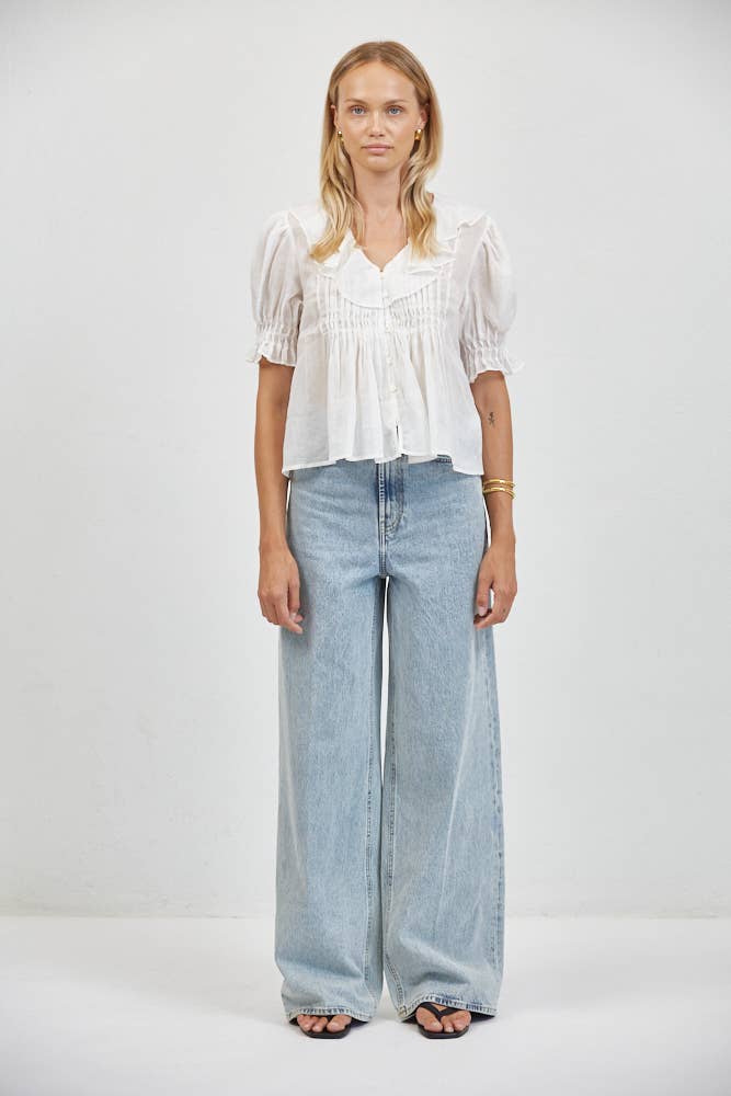 Woman in a short-sleeve cream top and light blue wide-leg denim jeans stands against a white backdrop.