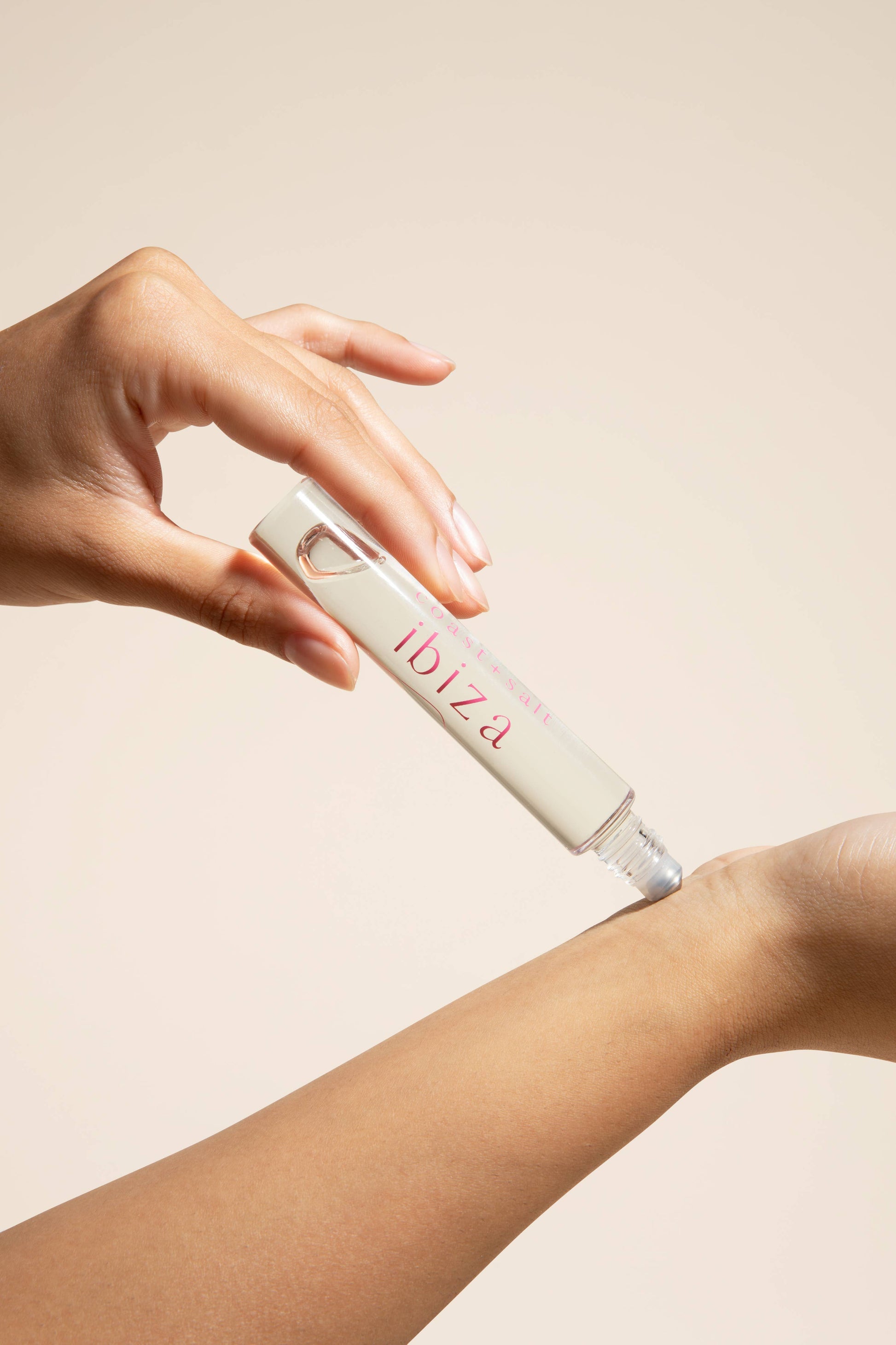 A hand rolls a clear glass perfume roller with a silver cap onto the inner wrist.