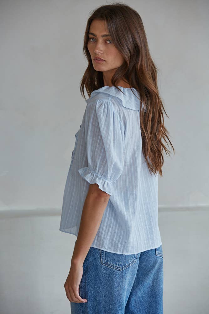Woman with long brown hair wears a powder blue knit top, shown in a side view, glancing toward the camera.