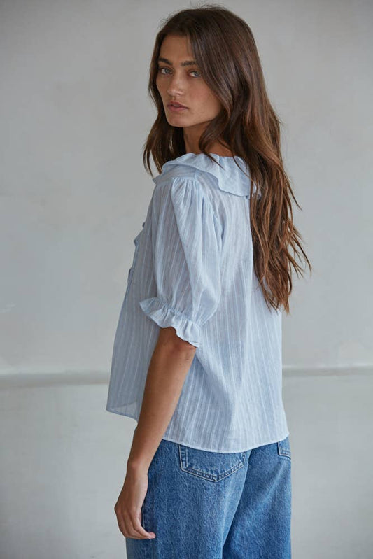 Woman with long brown hair wears a powder blue knit top, shown in a side view, glancing toward the camera.