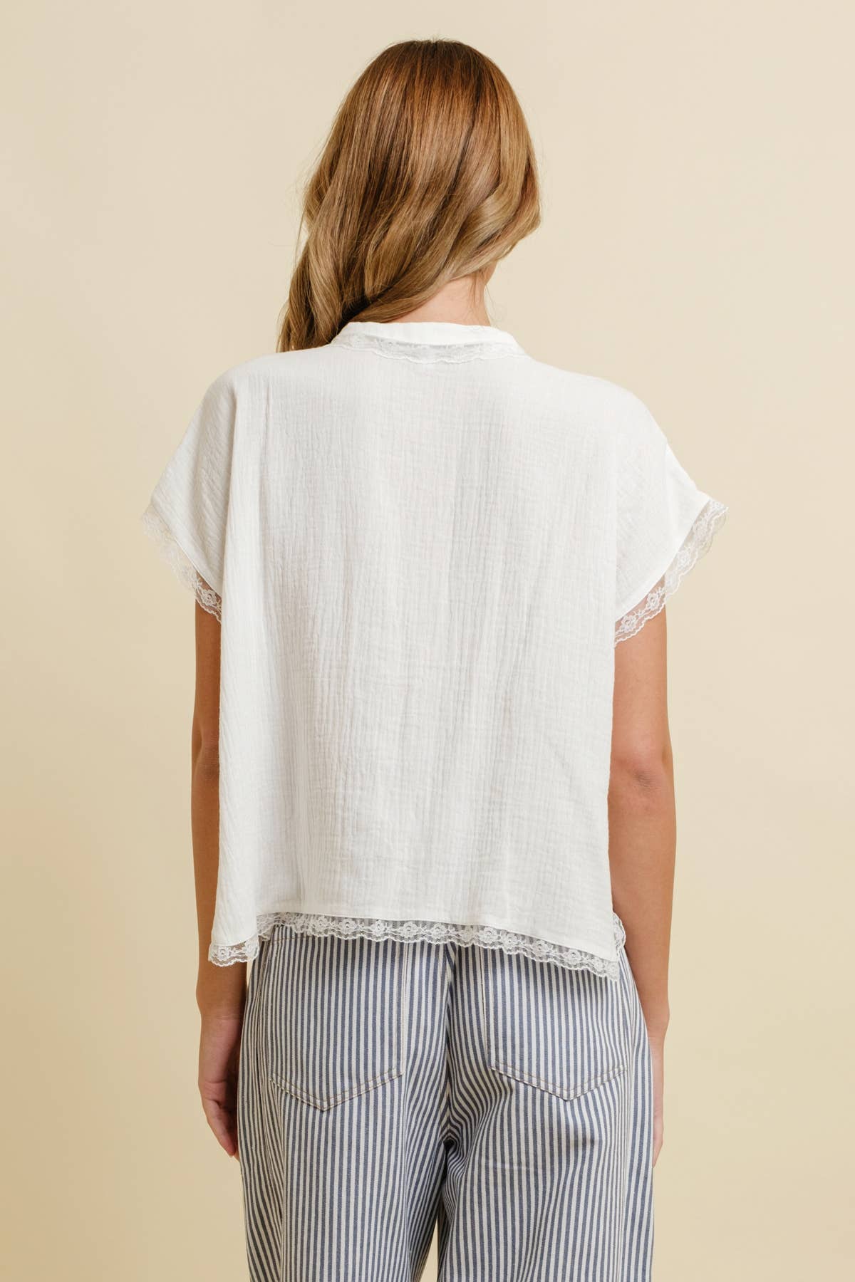 Woman seen from behind in a white tie-front lace-trim top and blue-and-white striped cotton pants.