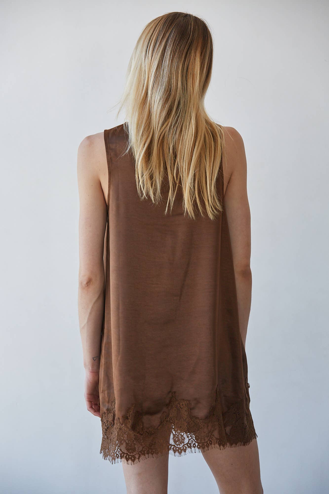Back view of a woman with long blonde hair wearing a brown mini dress, highlighting its shape and casual wear appeal.