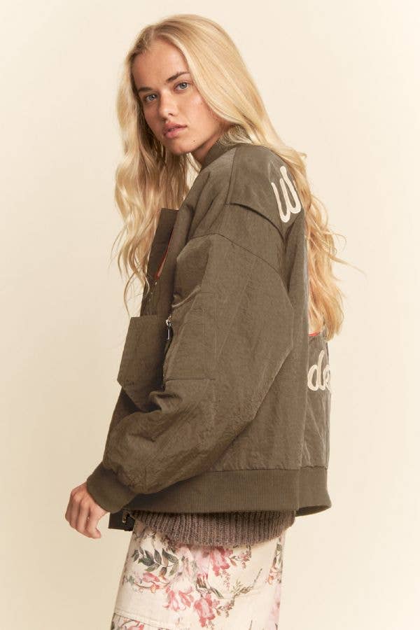 Blonde woman in embroidered bomber jacket, neutral background. Jacket features western details and likely cotton material.