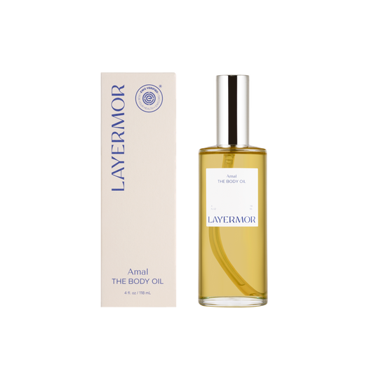 Clear glass bottle of body oil with cream-colored box on a white background; skincare product display.
