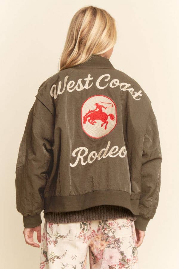 Woman in embroidered bomber jacket, featuring a red rodeo graphic on the back; jacket appears to be made of satin.