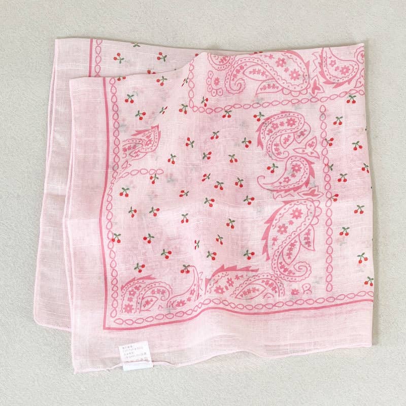 Pink paisley bandana with red cherry patterns, made of fabric, suitable as a stylish neck or hair accessory.