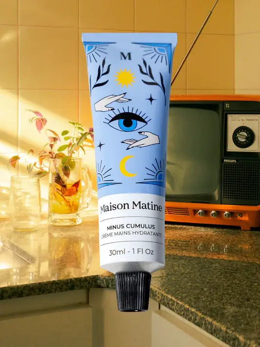 A tube of white hand cream rests on a kitchen counter near a TV, glass of water, and leafy green plant.