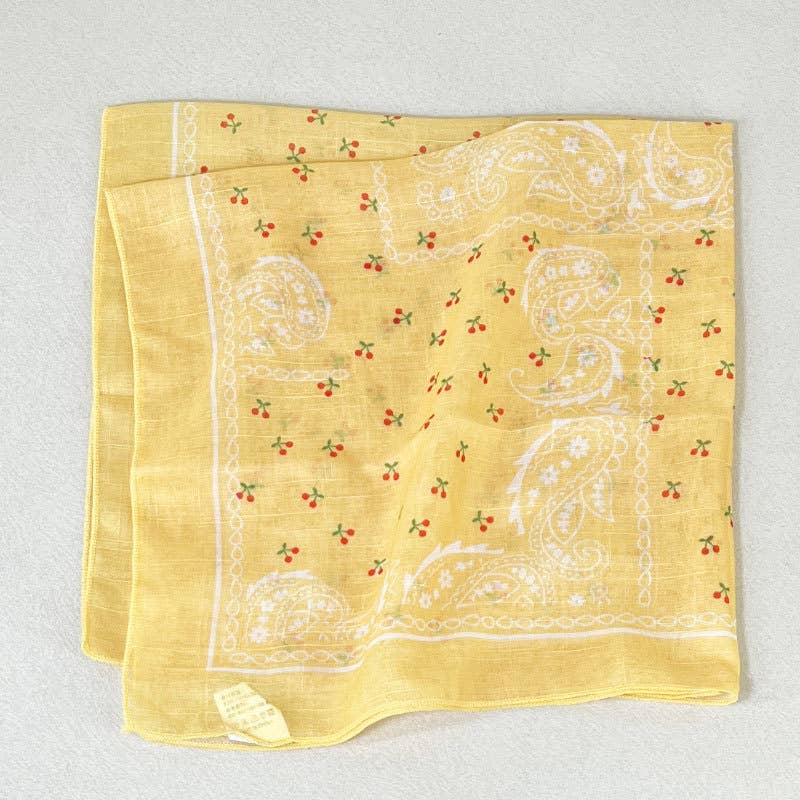 Yellow cotton bandana, folded, with white paisley pattern and multicolor accents; suitable for head or neck wear.