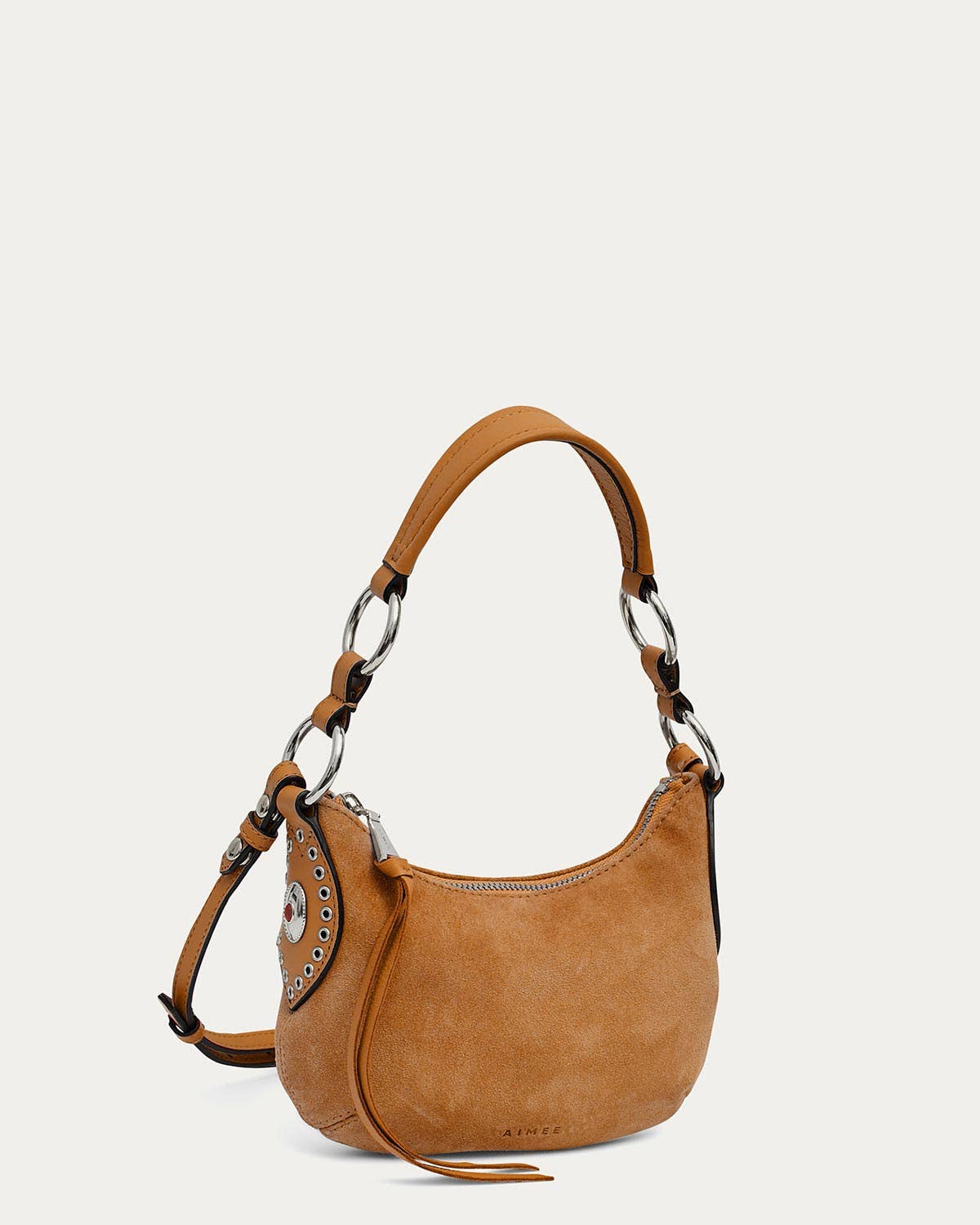 Latte suede crossbody bag with silver hardware, bold strap, eyelets, and zipper on a plain background.
