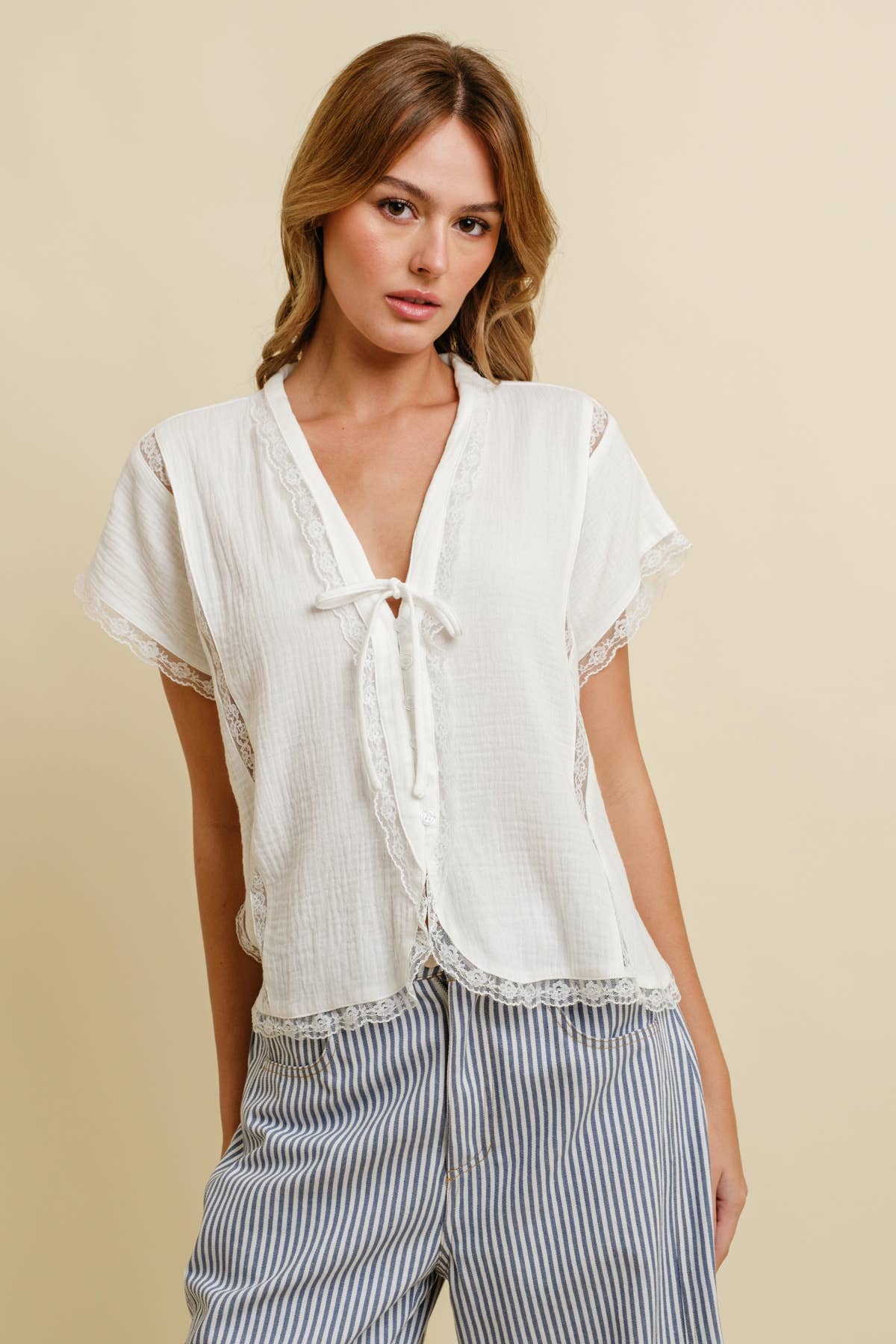Woman wears a white cotton top and striped pants, standing against a plain beige background.