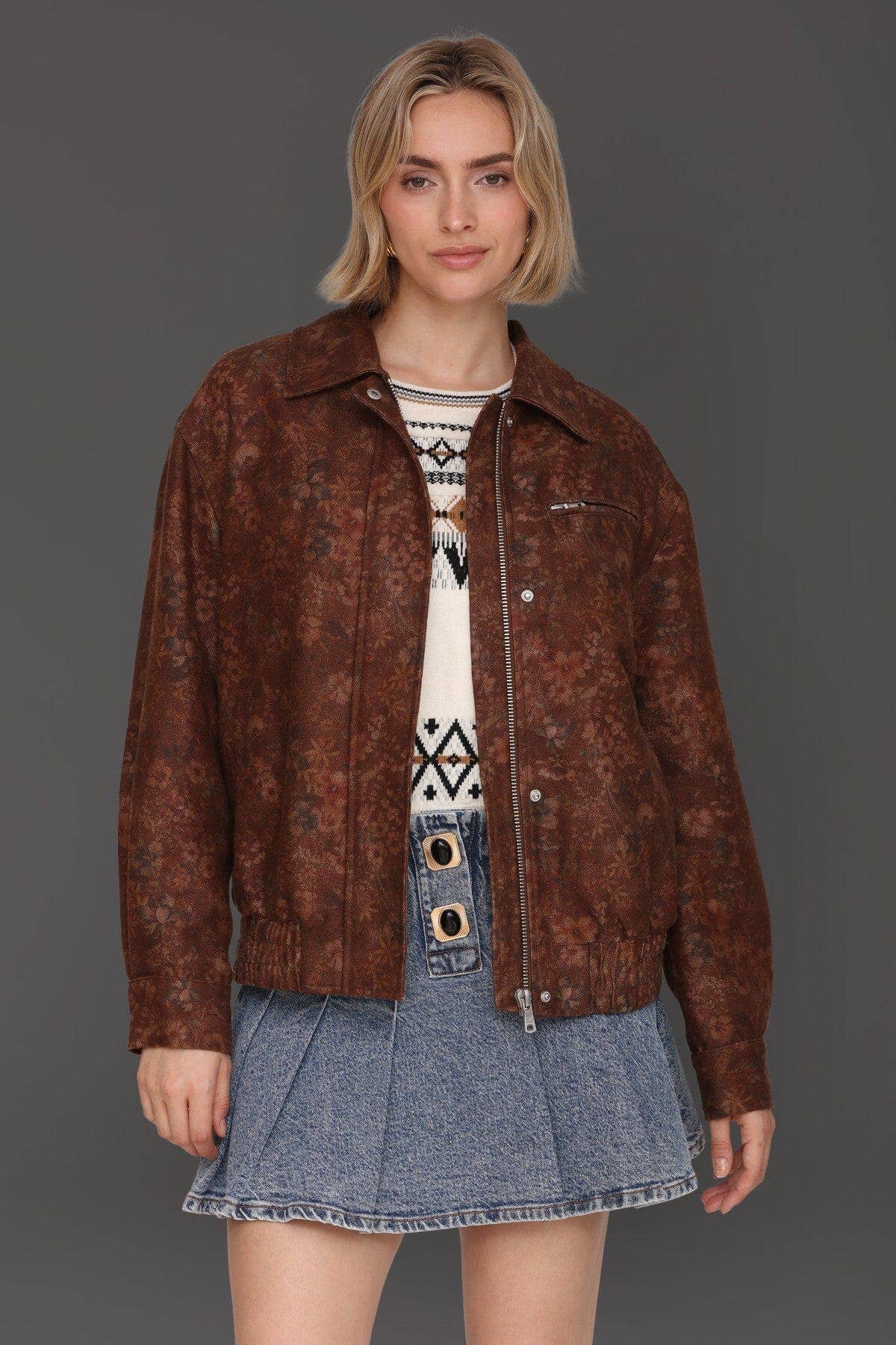 Woman wearing a floral print bomber jacket, white sweater, and blue pleated denim skirt.