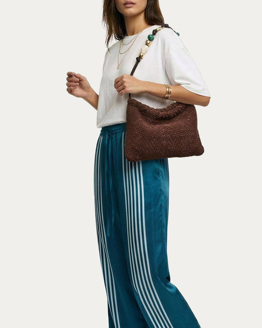 Woman wearing white shirt, striped pants, and gold jewelry with a leather shoulder bag in use.