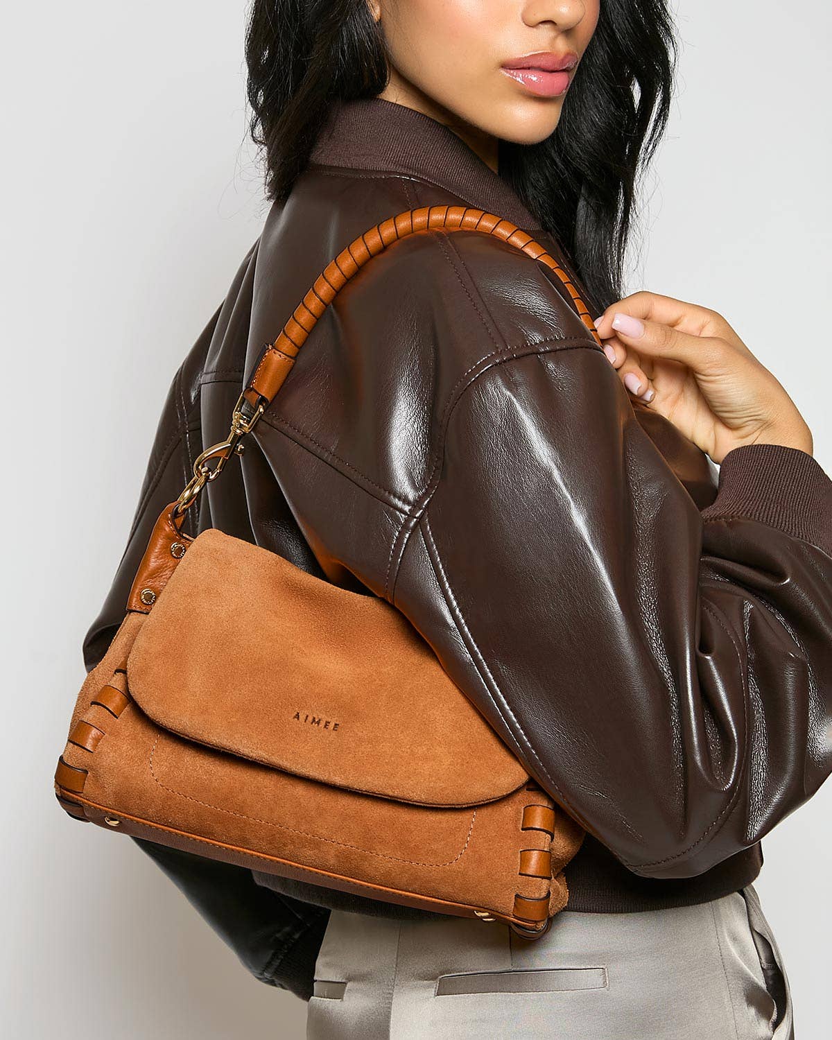 Woman in a brown leather jacket with a tan woven-handle crossbody bag worn on her shoulder.