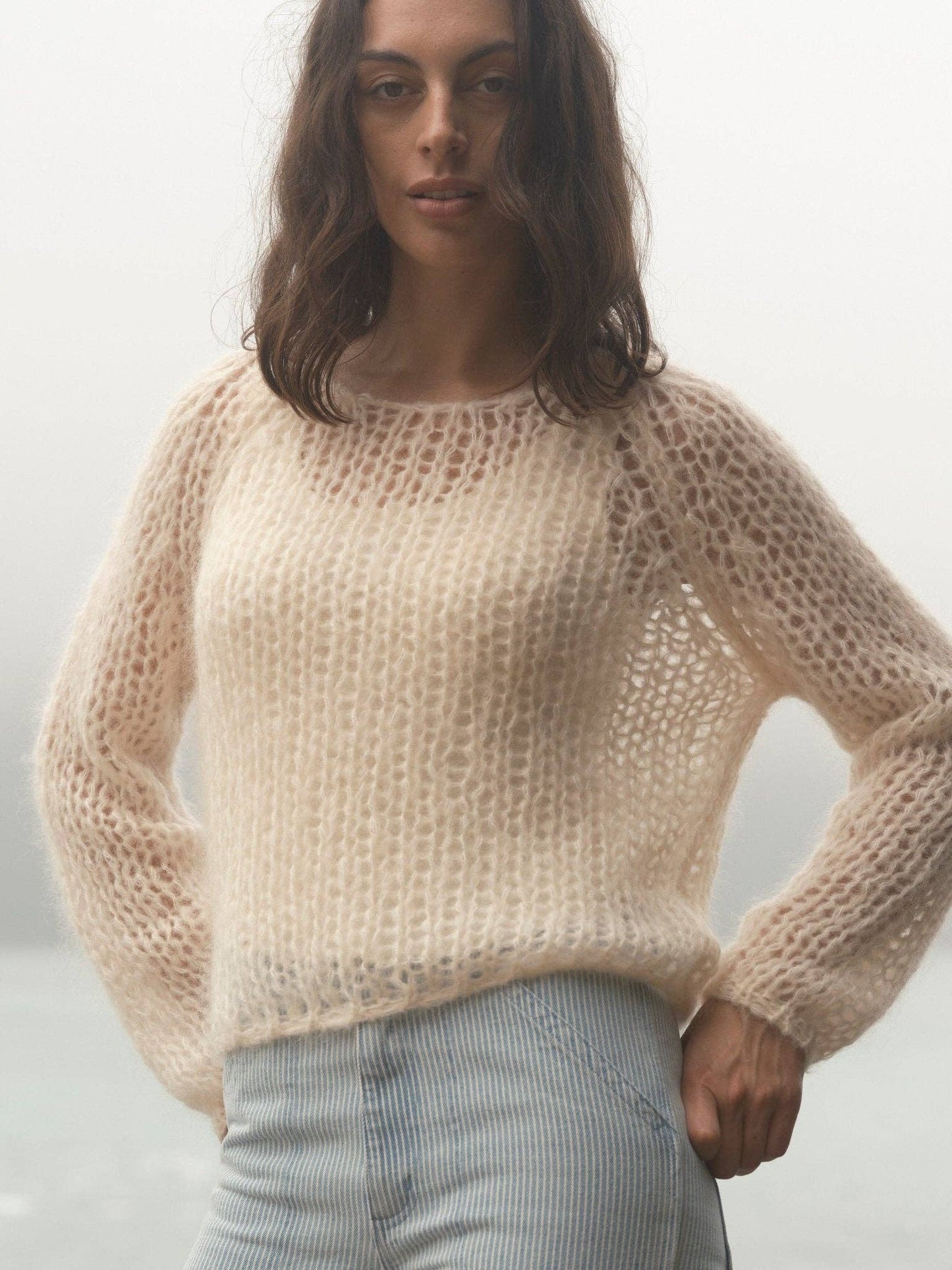 Woman outdoors in fog wearing sheer cream sweater and striped pants, highlighting light layering for cool weather.