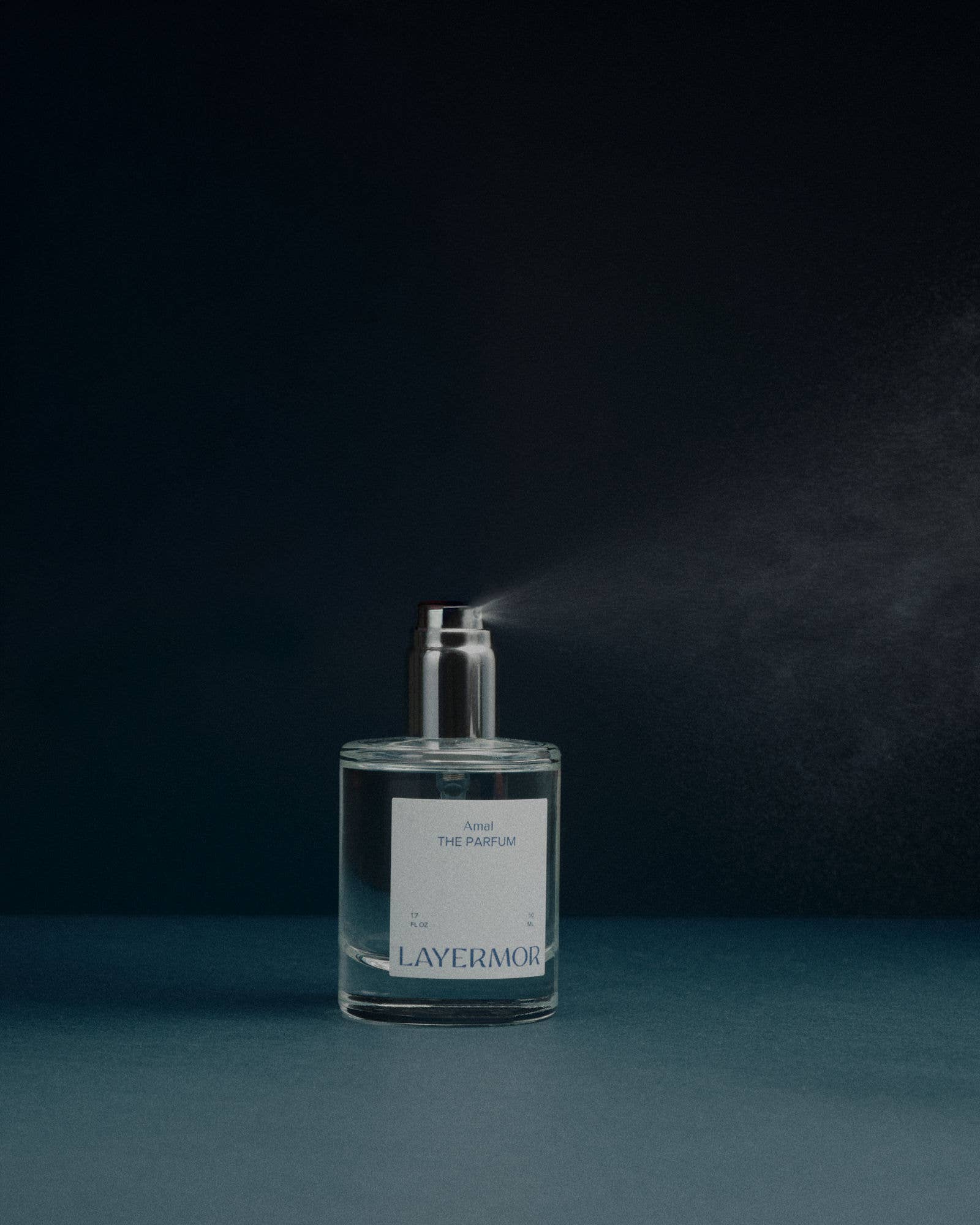 Transparent glass Layermor Amal perfume bottle sprays a fine mist, featuring a minimalist label and sleek design.