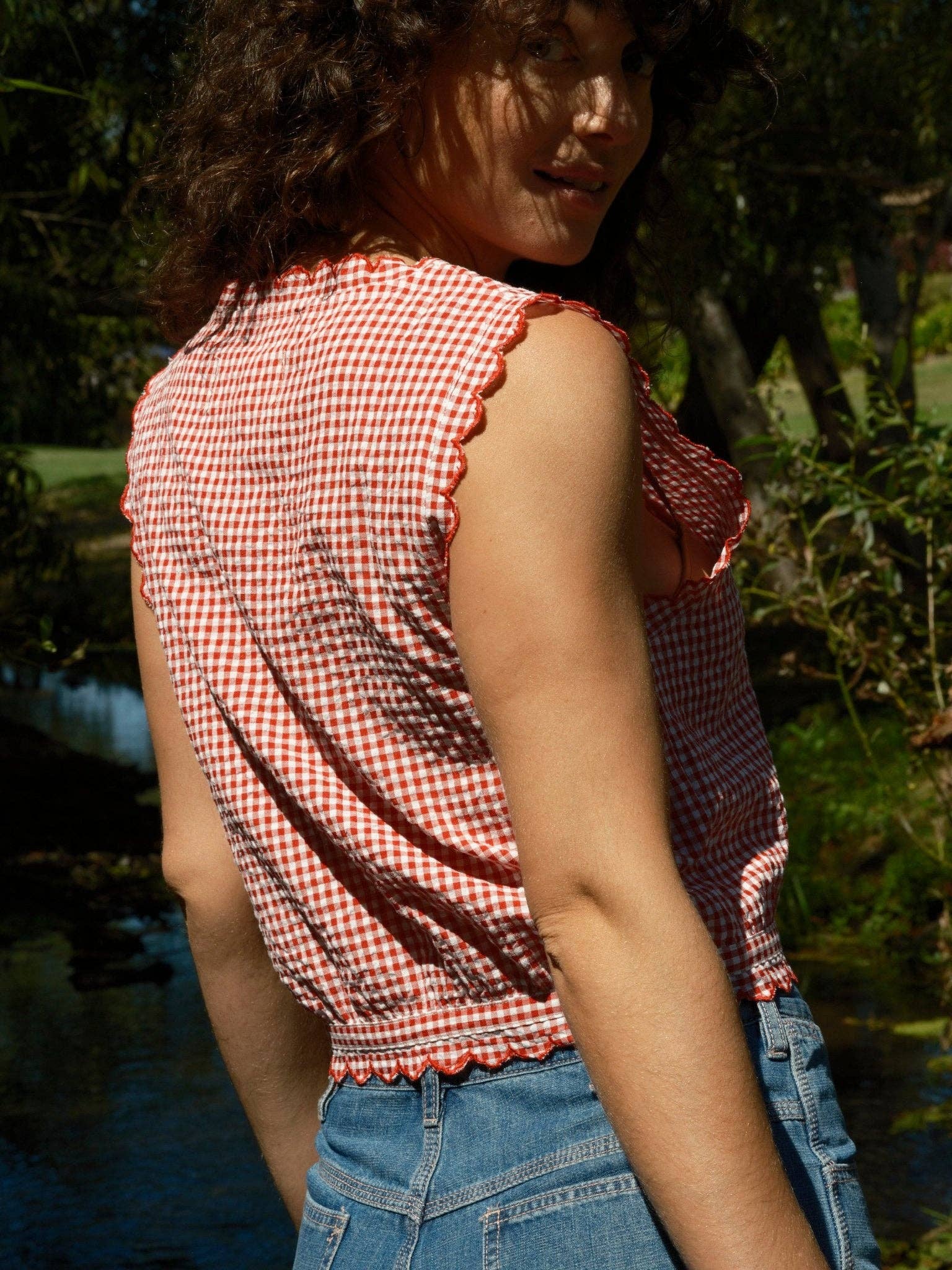 Red gingham sleeveless top with square neckline, worn outdoors by the water.
