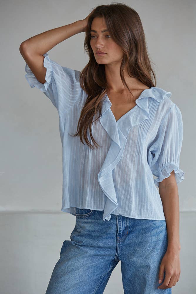 Powder blue top with jeans, soft fabric, modeled by a woman standing with one hand in her hair, looking sideways.