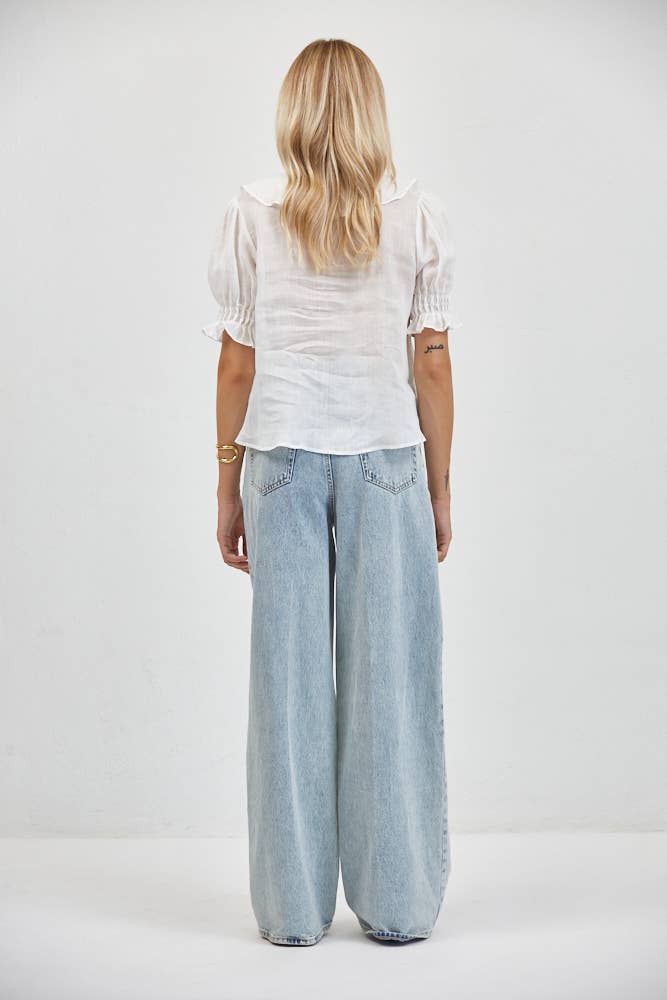 Woman in long blonde hair wears a white linen ruffle v-neck blouse with wide-leg jeans, styled for casual wear.