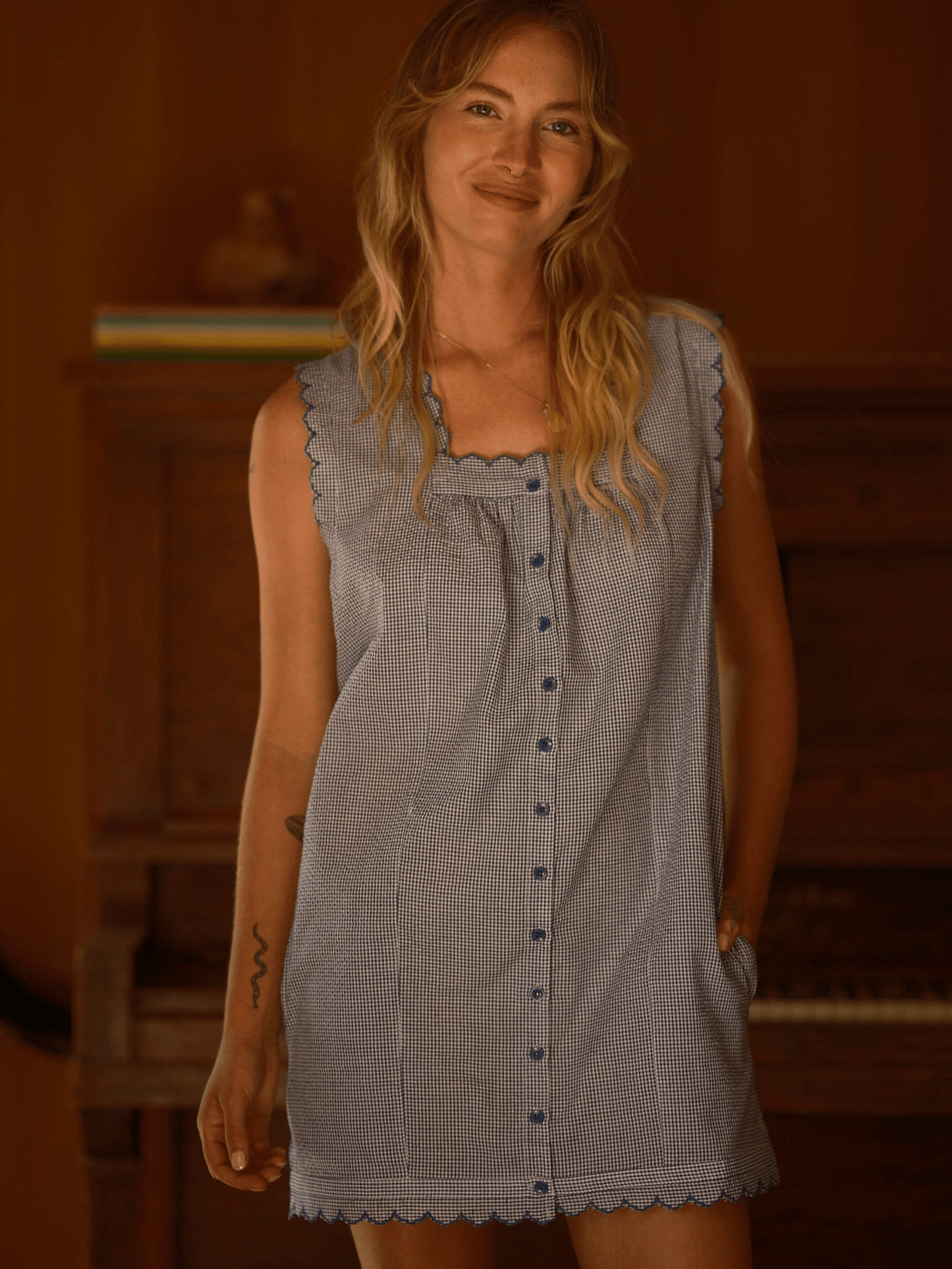 Woman wears a light-colored mini dress, likely cotton or linen, standing indoors near a piano.