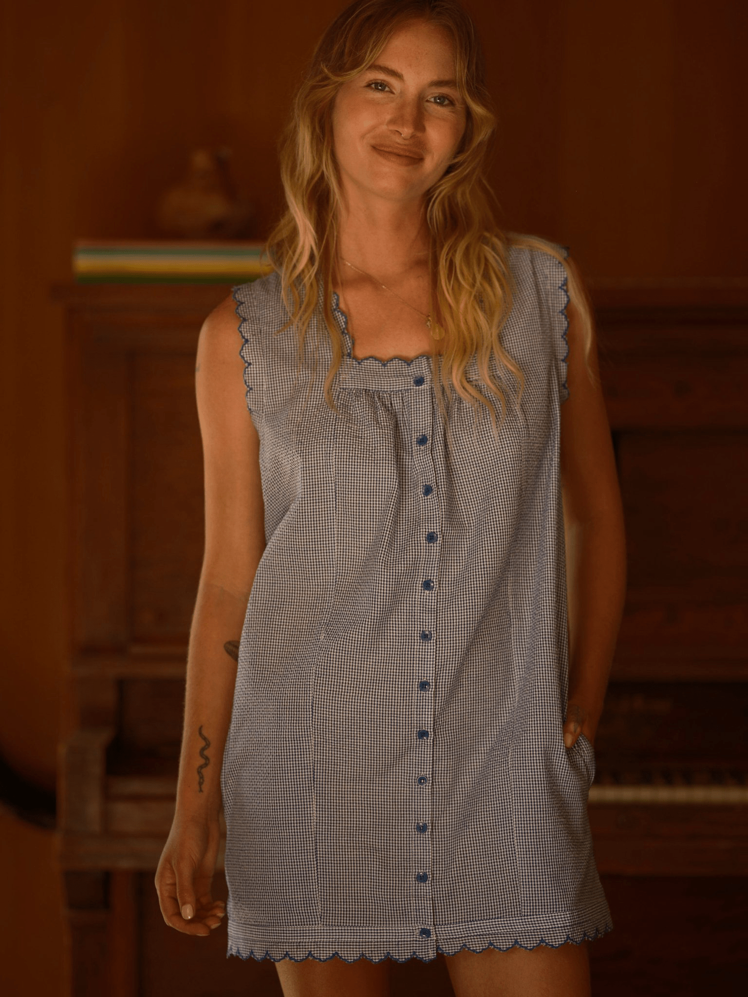 Woman wears a light-colored mini dress, likely cotton or linen, standing indoors near a piano.