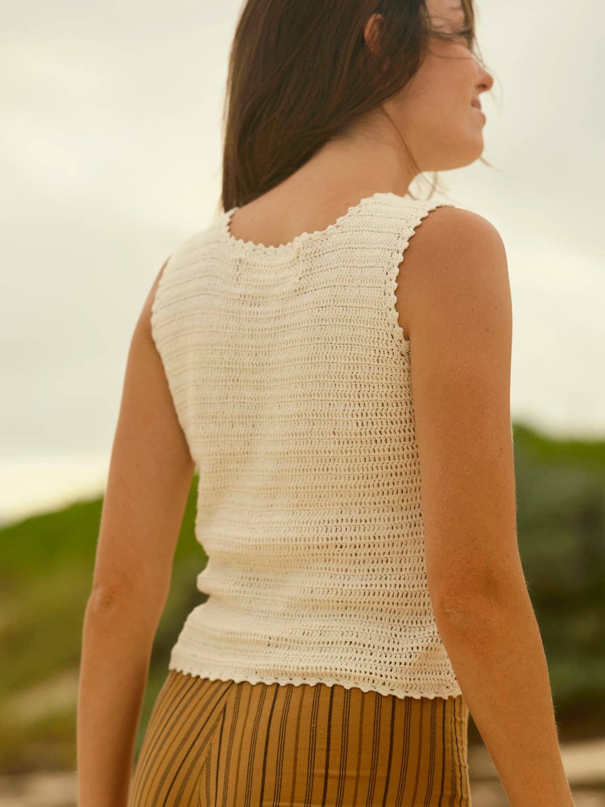 Woman wearing a white crochet tank and striped pants, standing outside. Features casual, airy fabric for warm weather.