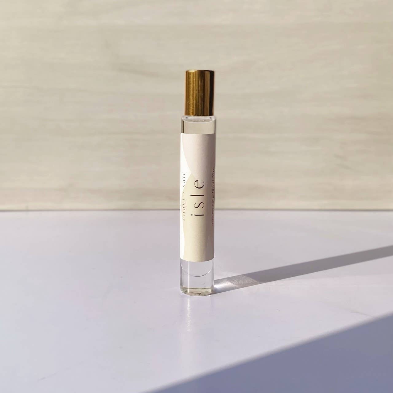 Coast+Salt Isle Perfume Roller with a gold cap rests on a white surface, designed for easy fragrance application.