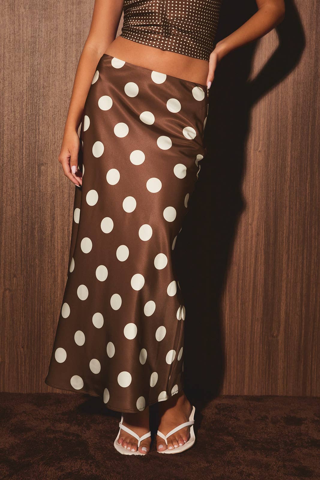 Woman in brown-white polka dot skirt, studded crop top, and white sandals, showcasing casual women’s attire.