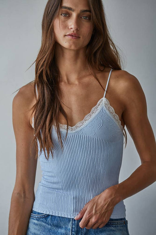 Woman in creamy blue Ava top and blue jeans, long brown hair, standing against a plain neutral background.