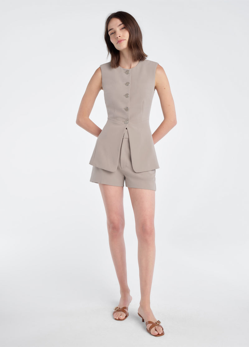 Woman in soft taupe mini shorts, sleeveless top, and brown sandals. Tailored cotton blend; ideal for warm weather casual wear.
