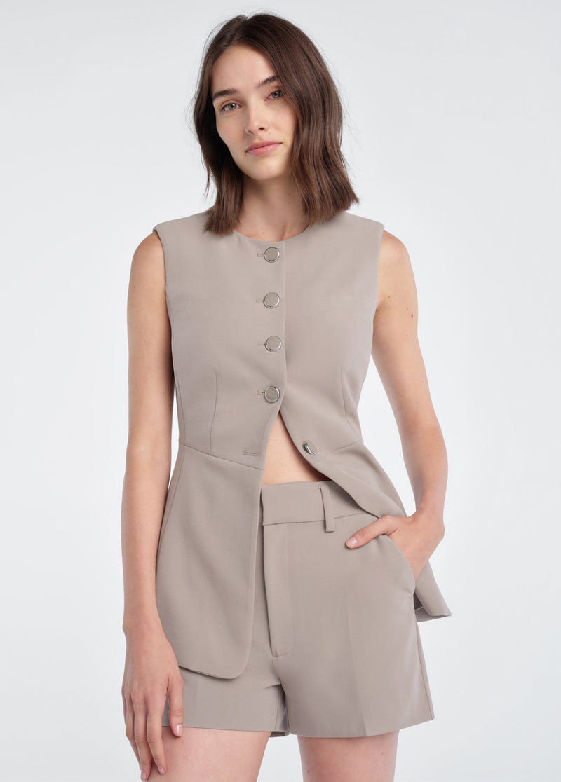 Woman in soft taupe mini shorts and a sleeveless blazer, showcasing tailored summer wear.