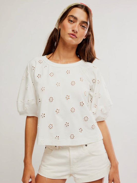 Woman in a white eyelet cotton tee and matching white shorts, standing against a plain backdrop.