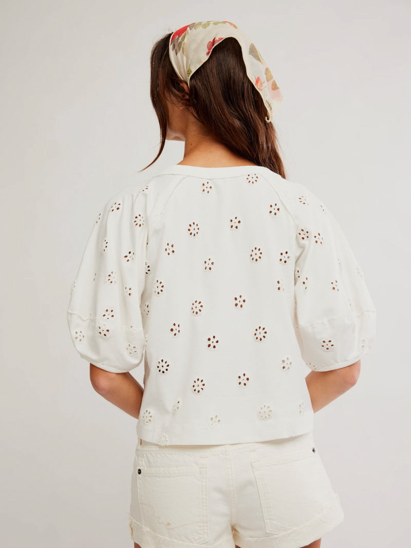 Back view: woman in white eyelet tee, shorts, and a floral hair scarf. Cotton top with embroidered details.