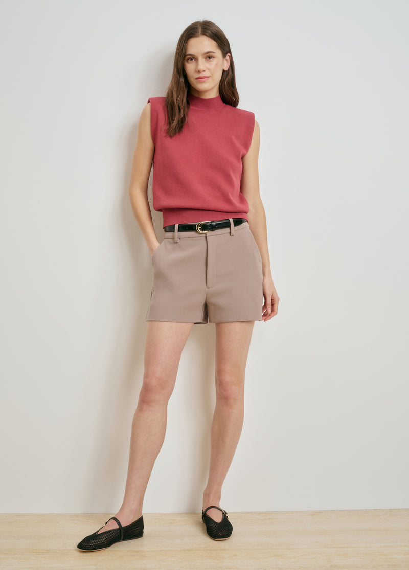 Woman in soft taupe mini shorts, red sleeveless top, and black belt, showcasing versatile warm-weather attire.
