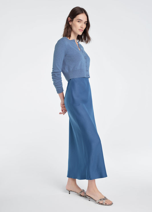 Woman in a blue cropped cardigan over a satin slip dress, paired with low-heeled sandals.