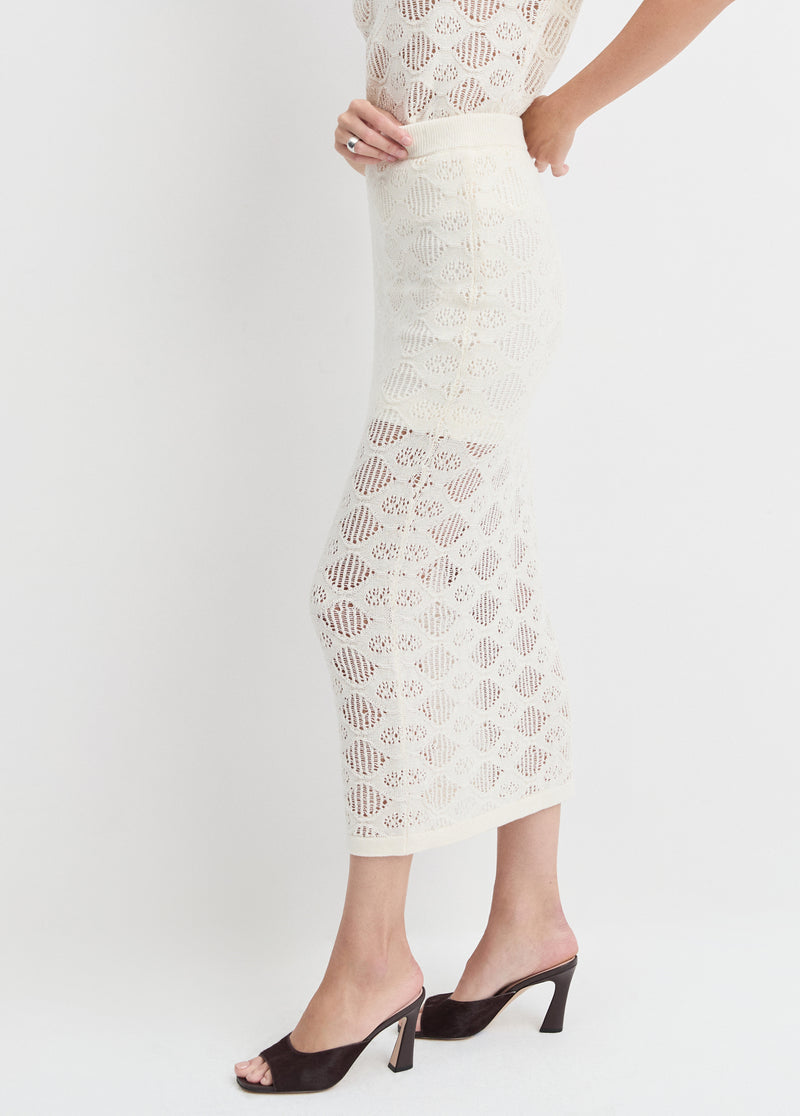 Woman in ivory skirt and matching top, made of lightweight fabric, with black open-toe heeled sandals, shown sideways.