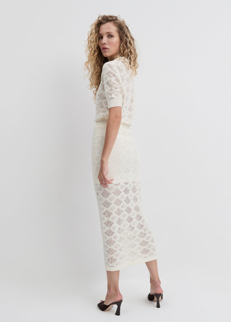 Woman with curly hair wears an ivory cotton polo shirt, suitable for casual or semi-formal occasions, on a white backdrop.