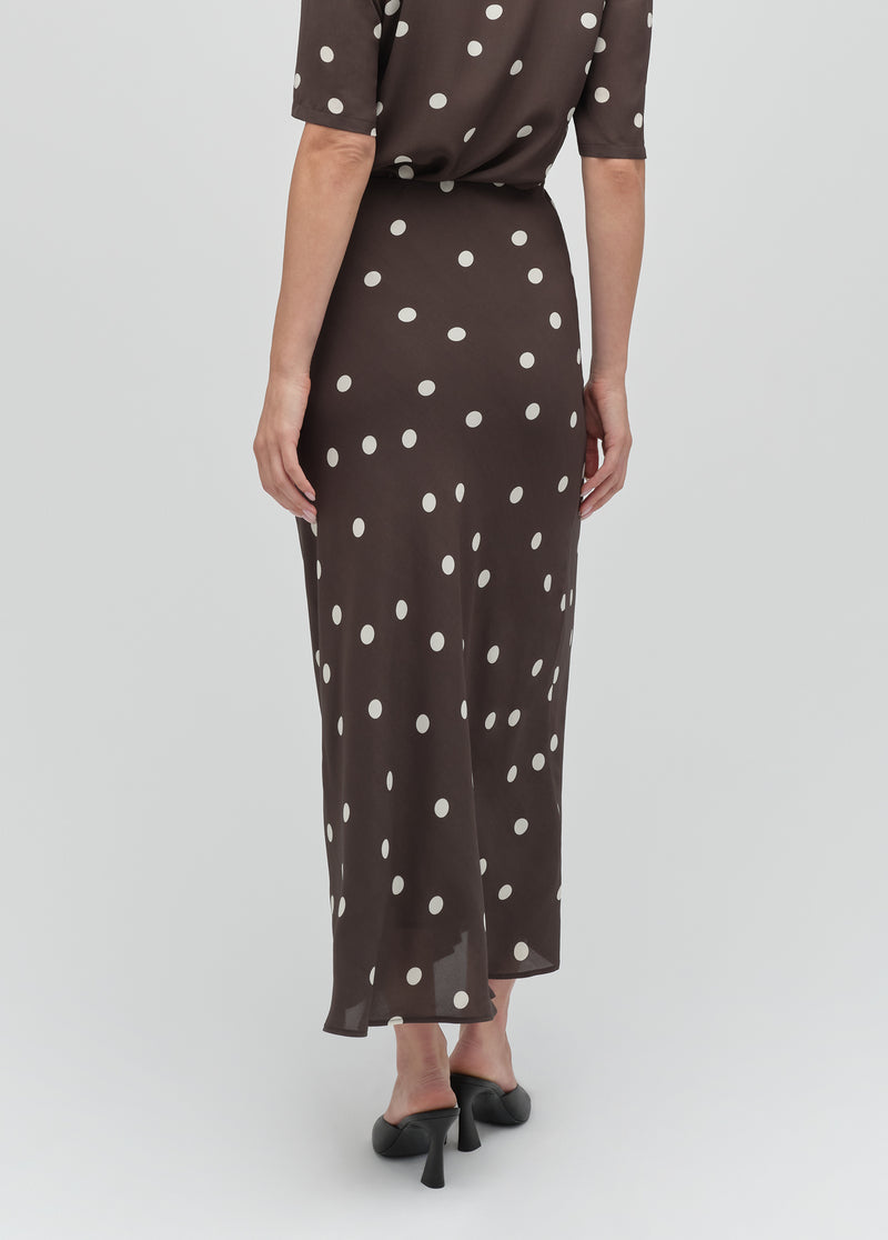 Back view of a woman in a brown polka dot skirt with black heels, highlighting the garment’s fit and pattern.