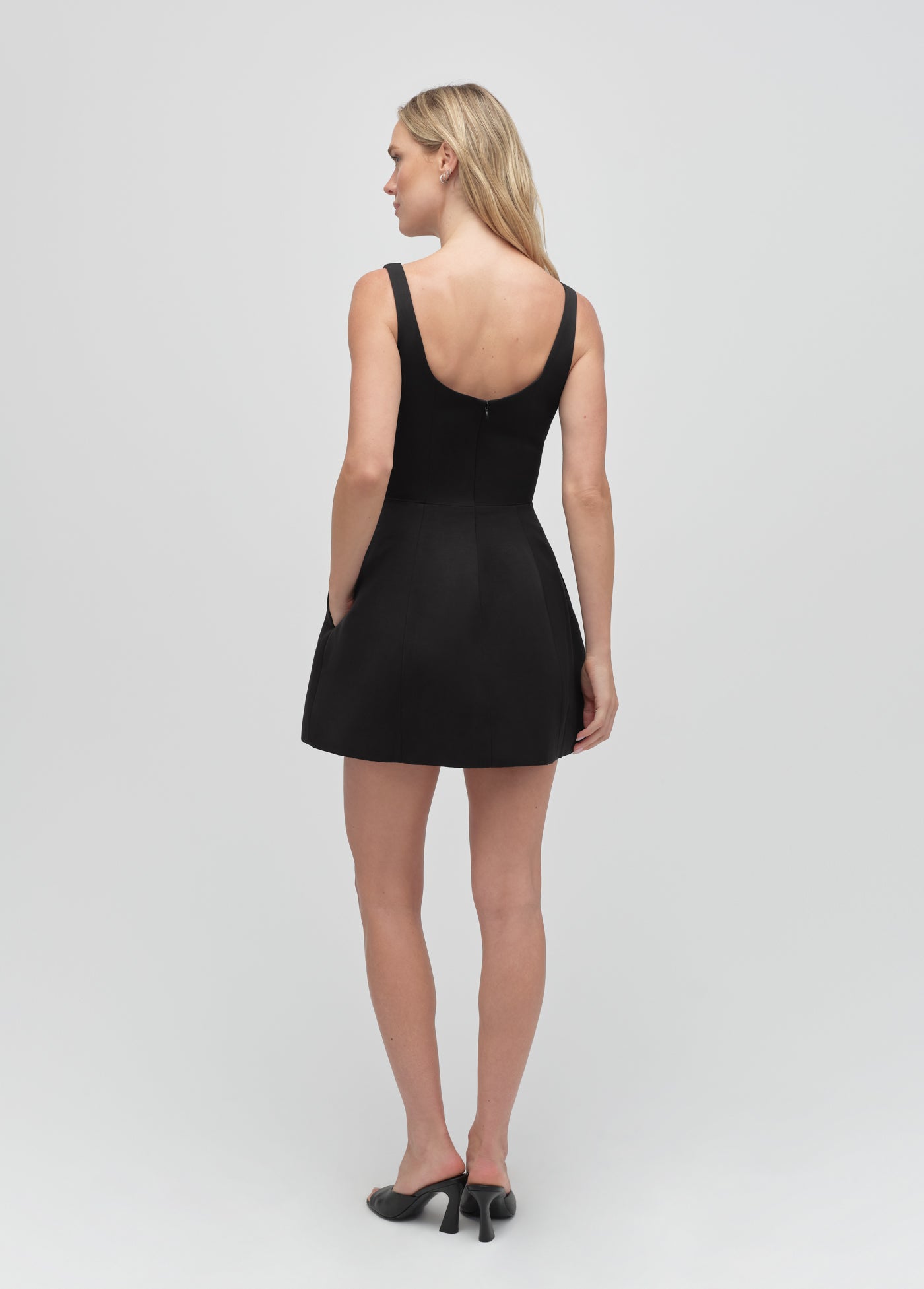 Woman models a black sleeveless dress, shown from the back against a plain light background.