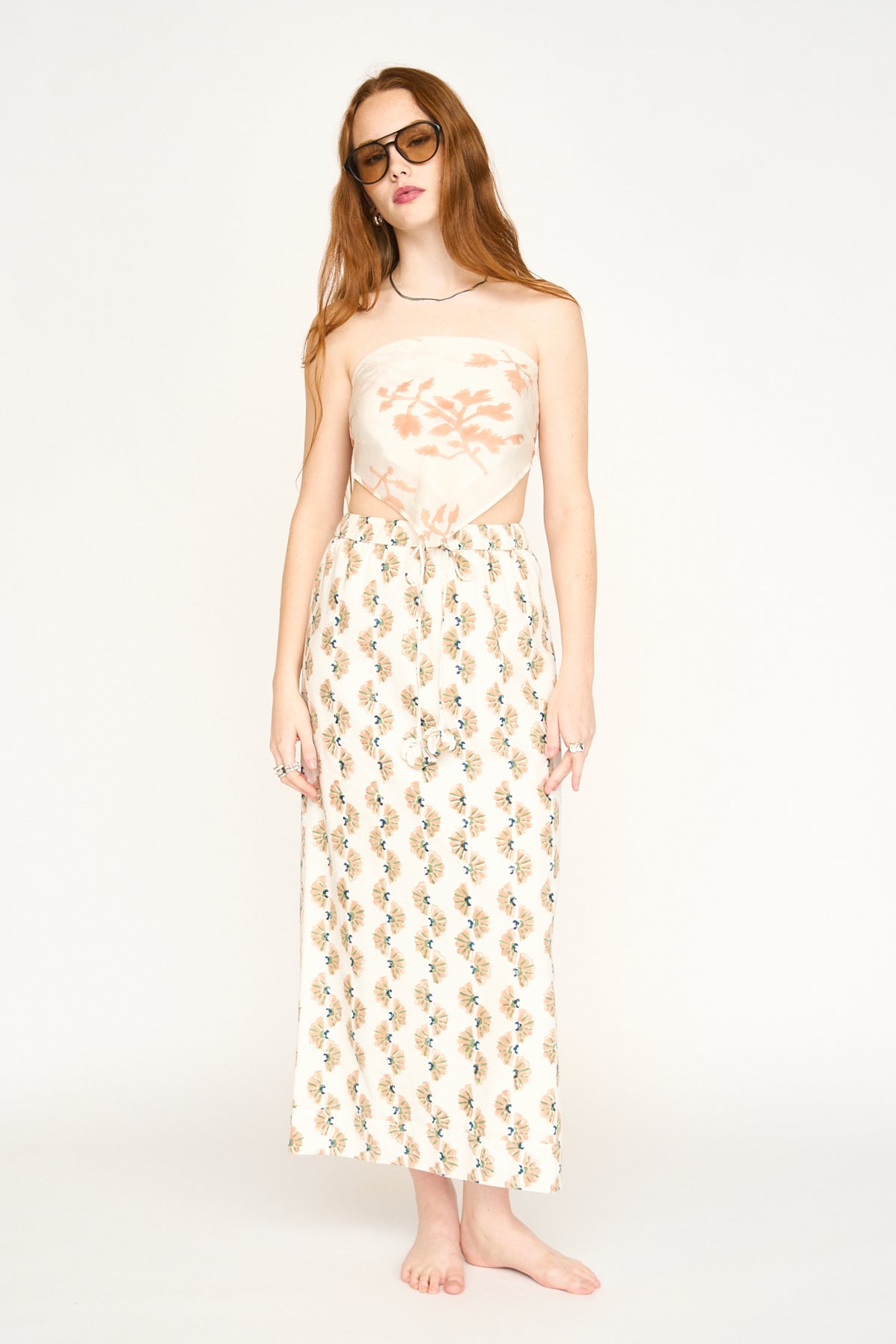 Red-haired woman in sunglasses models a Mesa Fig cotton bandana, barefoot before a plain white backdrop.