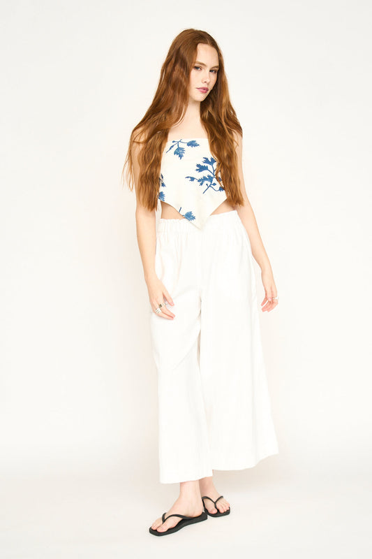 Woman with long red hair wears a floral bandana in Summer Fig, a patterned blouse, white pants, and black sandals.